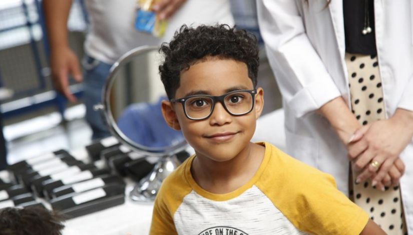 Fotografia de um menino usando óculos. Ele olha para câmera comum leve sorriso.