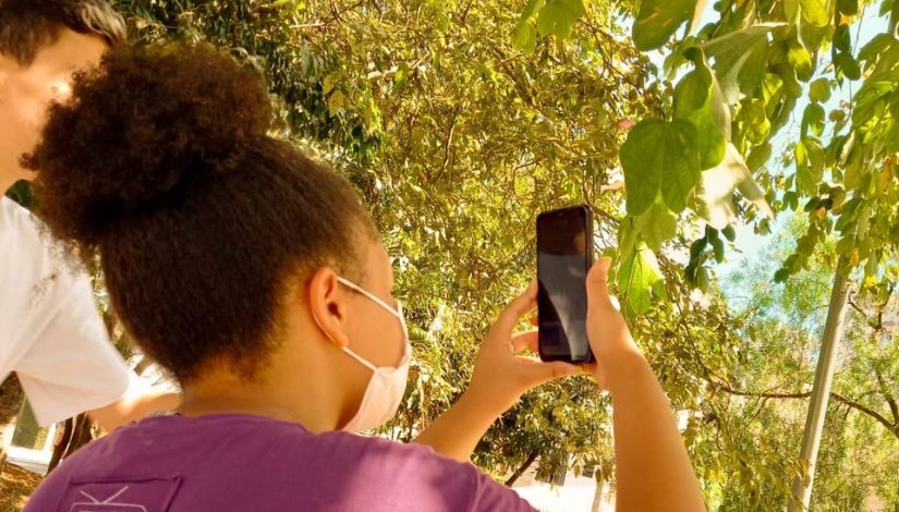 fotografia de garota apontando a câmera do celular para uma vegetação 