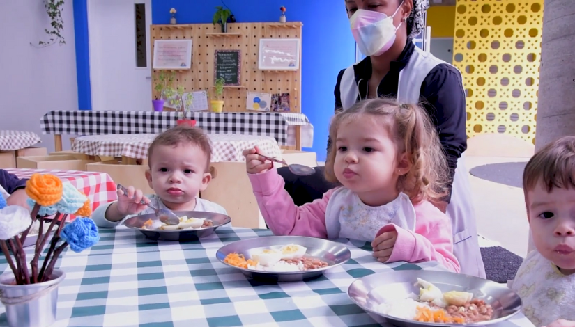 foto com 3 crianças pequenas em destaque, comento com colher, no prato, arroz, feijão, ovo e cenoura ralada