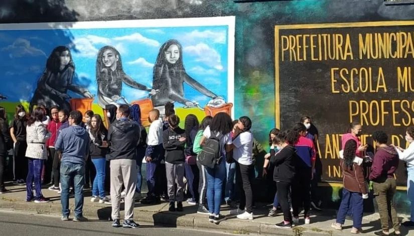 Fotografia de um muro com grafite e várias pessoas na calçada observando a arte.