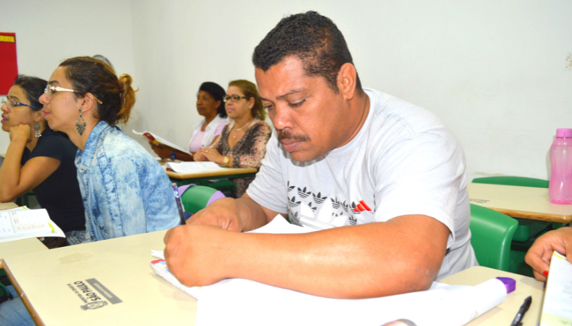 fotografia de um ambiente escolar com estudantes jovens e adultos. Em destaque, um homem com cerca de 40 anos