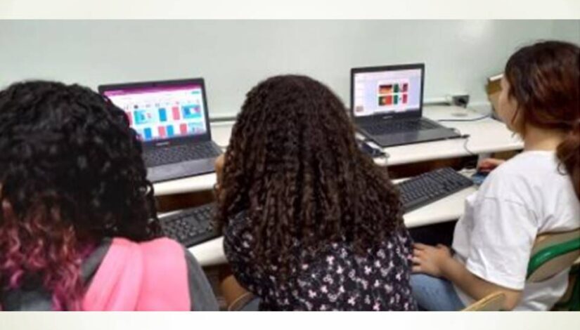 Foto de 3 meninas, de costas, mexendo em 2 notebooks