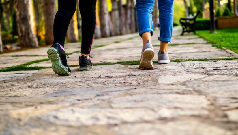 Imagem de duas pessoas do joelho para baixo em movimento de caminhada em um parque.