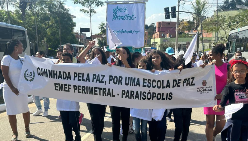 Fotografia mostra estudantes de pé segurando uma faixa onde está escrito "Caminhada pela paz, por uma escola de paz - EMEF Perimetral - Paraisópolis".