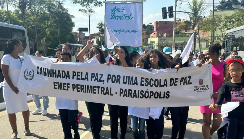 Fotografia mostra estudantes de pé segurando uma faixa onde está escrito 