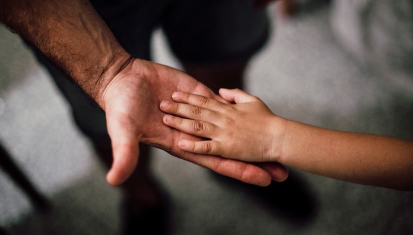 Fotografia de uma mão masculina tocando uma mão de criança