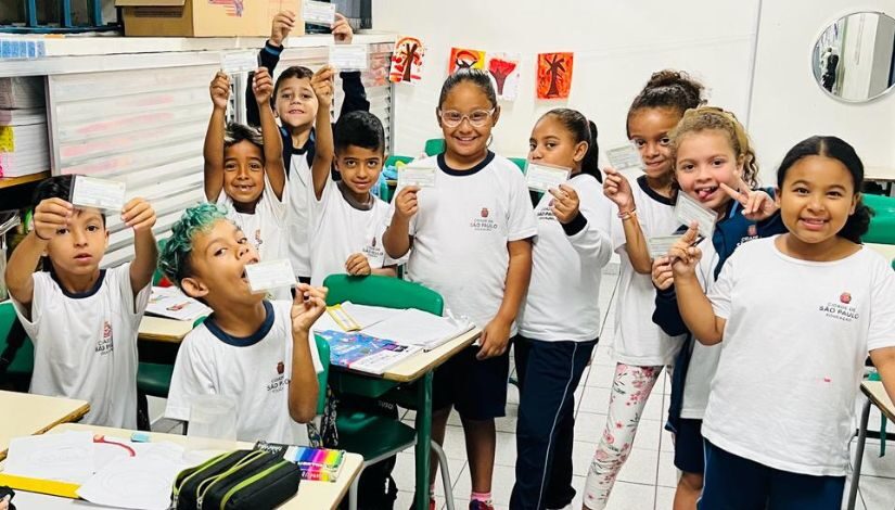 Crianças posando para a foto com seus títulos de eleitores em mãos.