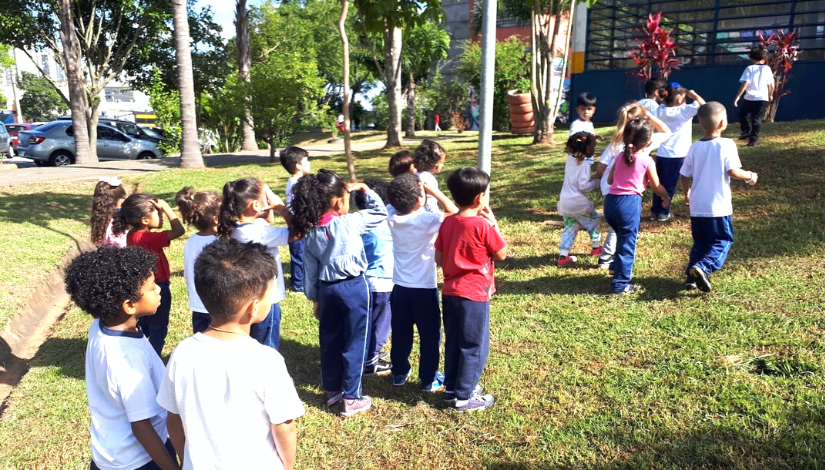 Crianças estão em área verde de costas para a foto.