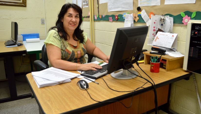 foto de uma mulher atrás de uma mesa com computador e papéis