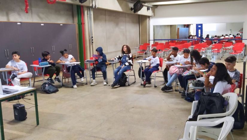 Estudantes estão sentados em círculo em uma sala de aula.