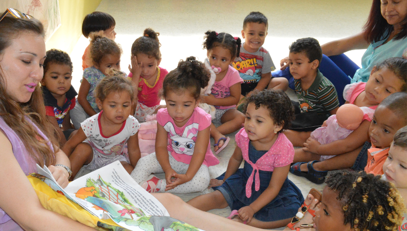 foto de uma professoras lendo um livro para bebês que estão sentados a sua volta