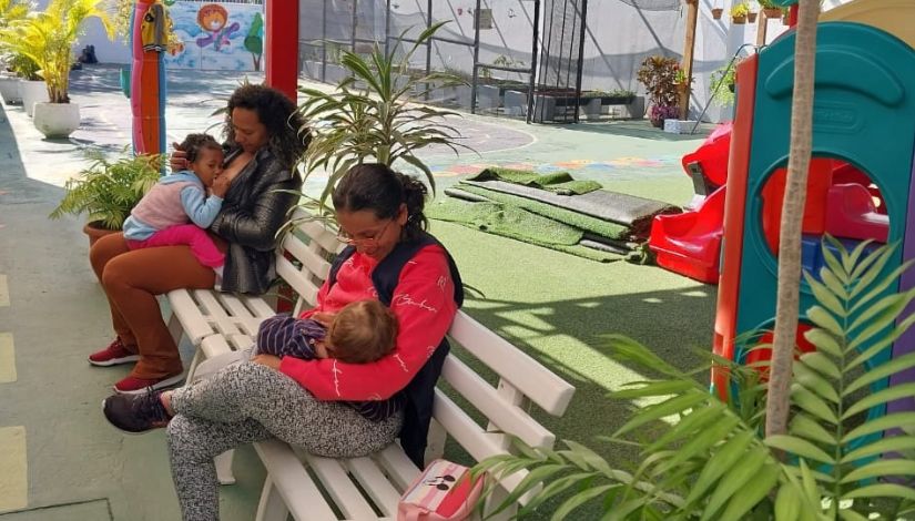 Fotografia de duas mulheres sentadas amamentando suas crianças em área externa da unidade educacional.