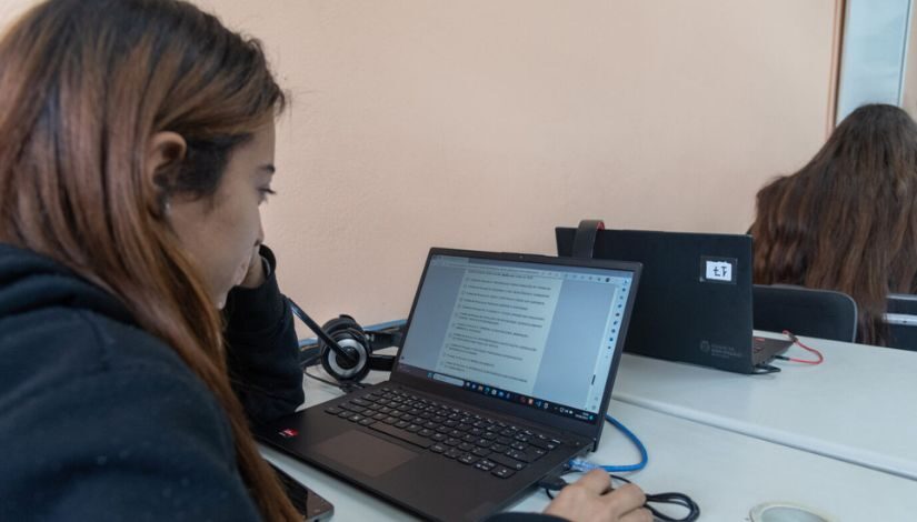 Menina de frente para um notebook com uma das mãos sobre um mouse. 