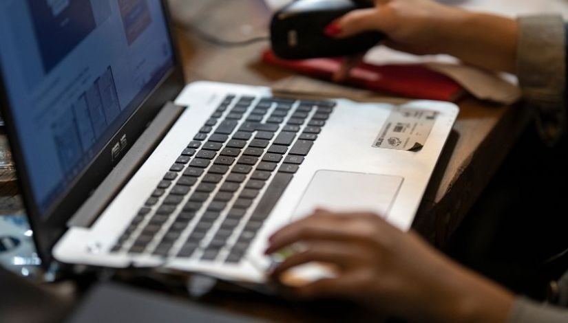 Imagem de um computador portátil e as mãos de uma pessoa sobre ele.