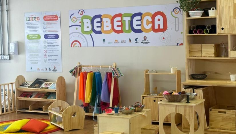 Espaço com brinquedos e prateleiras de madeira. Ao fundo há uma placa onde está escrito "Bebeteca".