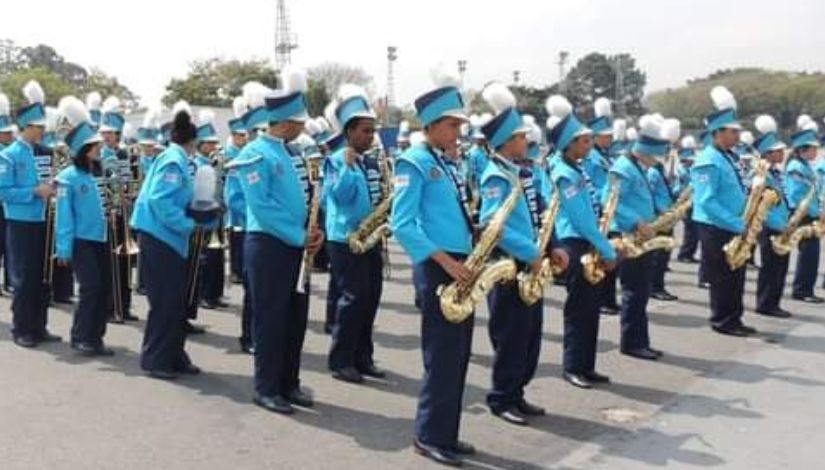 Foto de estudantes com roupa de desfile cívico, tocando saxofone