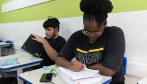 Dois estudantes sentados escrevendo em seus cadernos na sala de aula