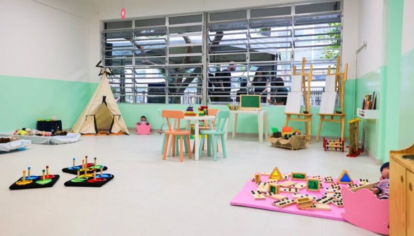 Fotografia de uma sala do CEI Ibirapuera com brinquedos, mesa e cadeiras pequenas de madeira, cabana de pano, entre outros.