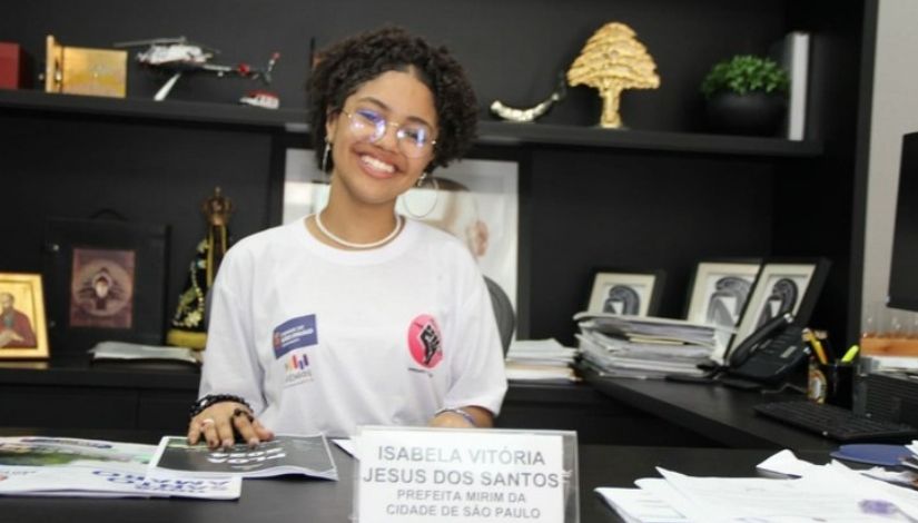 Foto de uma estudante Jovem, sentada e sobre a mesa, a descrição Isabela Vitória, Prefeita Mirim da cidade de São Paulo