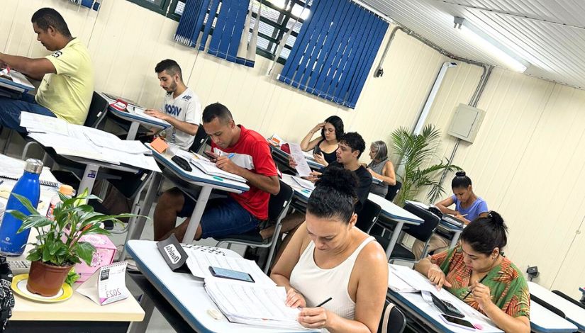Fotografia mostra estudantes sentados escrevendo em seus cadernos sobre suas mesas. Eles são alunos do curso de Recursos Humanos, do Centro Municipal de Capacitação e Treinamento (CMCT).