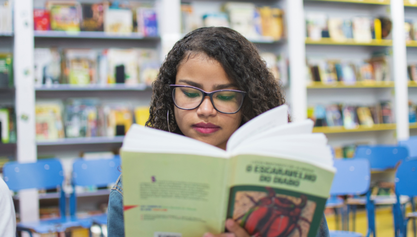 Fotografia de uma garota fazendo leitura de um livro em uma sala de leitura