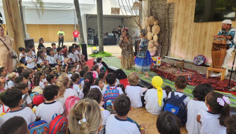 Fotografia de estudantes sentados no chão assistindo a um apresentação cultural. 