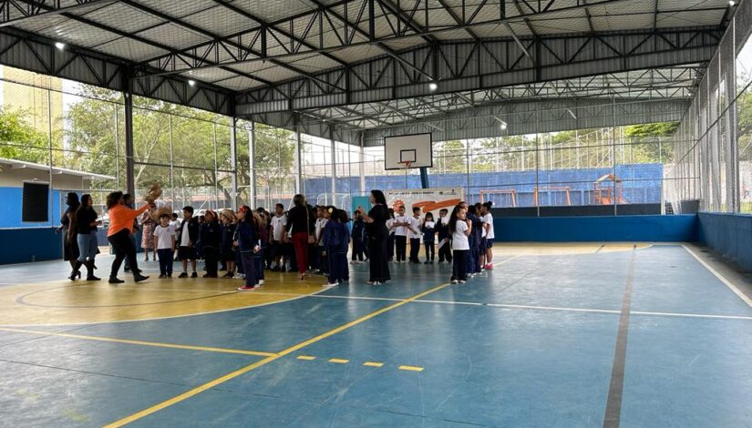 Fotografia de uma quadra coberta e estudantes e professores nela.