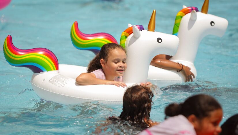 Fotografia de crianças na piscina com boias de unicórnio.