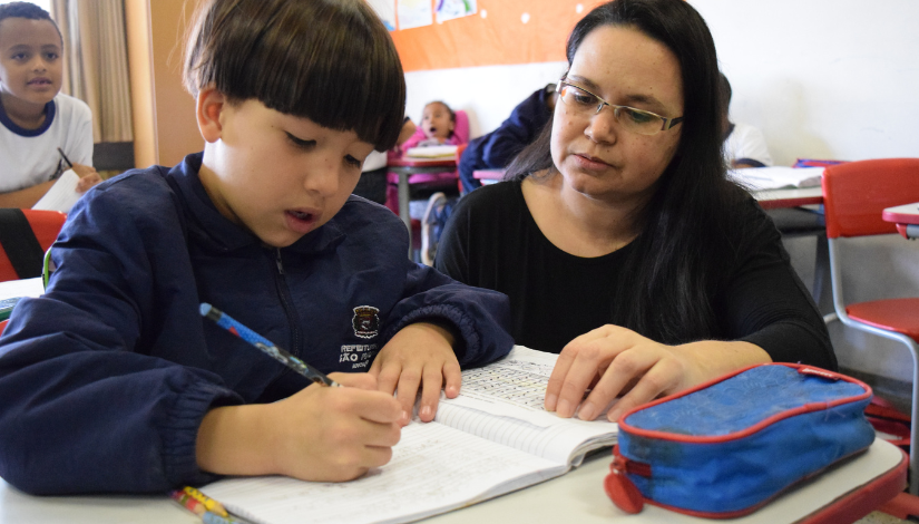 Professora De Ensino Fundamental Auxiliando um garoto na alfabetização