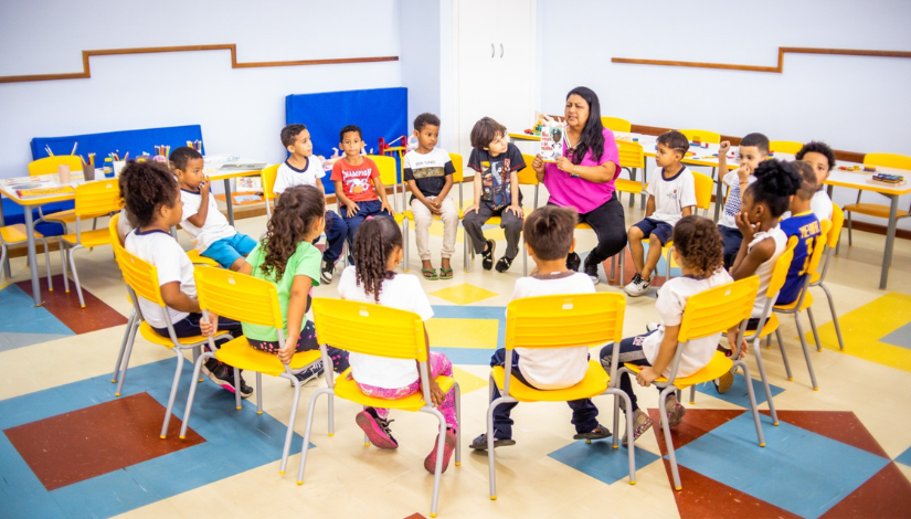 Foto de uma roda de contação de história com a professora e os estudantes em ambiente escolar.