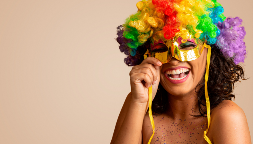 fotografia mostra uma mulher sorrindo com uma peruca colorida e segurando uma máscara na frente de seu rosto