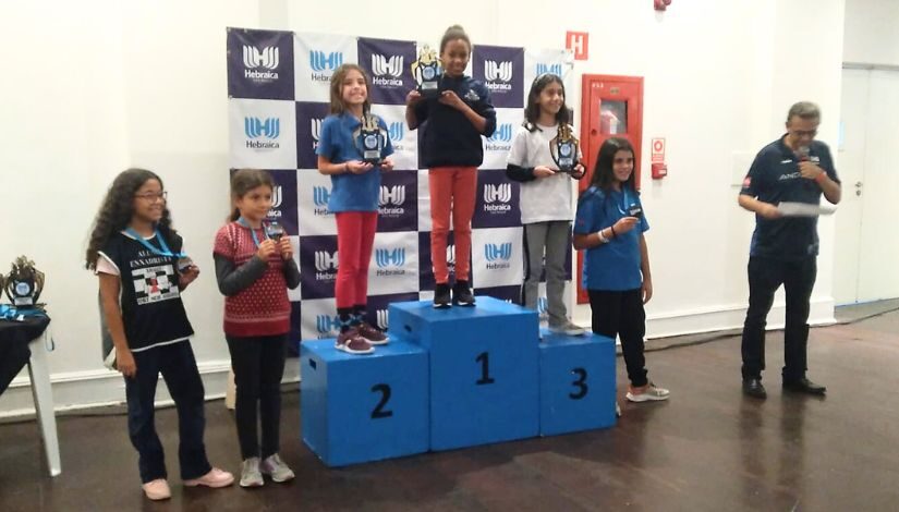 Fotografia mostra um pódio com a estudante Yara Nayelle da Cruz Costa, em 1º lugar - Campeã Paulista De Xadrez Sub 10 Femino.