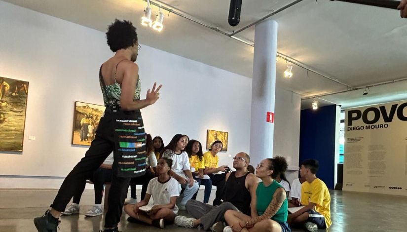 Estudantes sentados observando professor durante visita ao Museu Afro