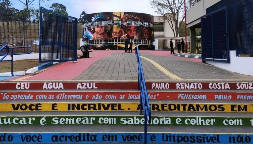 Fotografia mostra a escadaria dentro do CEU Água Azul e ao fundo um prédio em formato redondo com grafites de crianças.