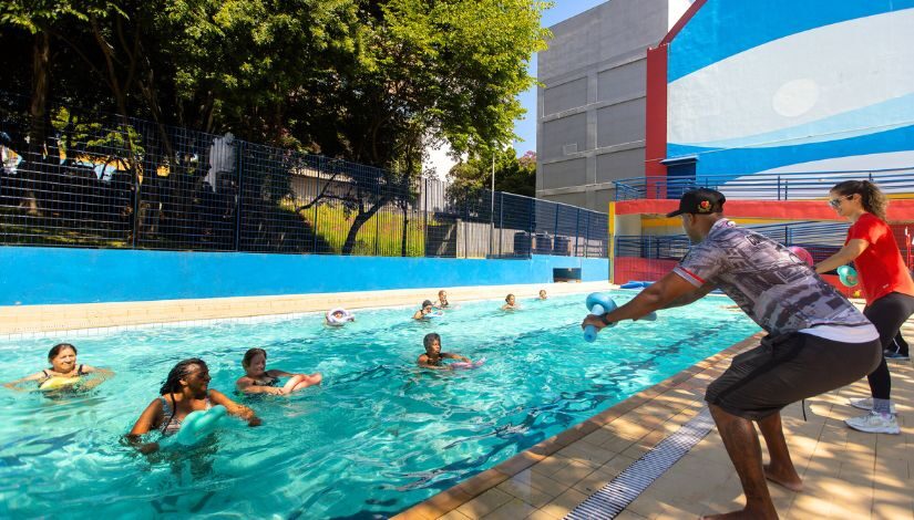 Fotografia mostra pessoas adultas dentro de uma piscina durante aula de hidroginástica no CEU Heliópolis.
