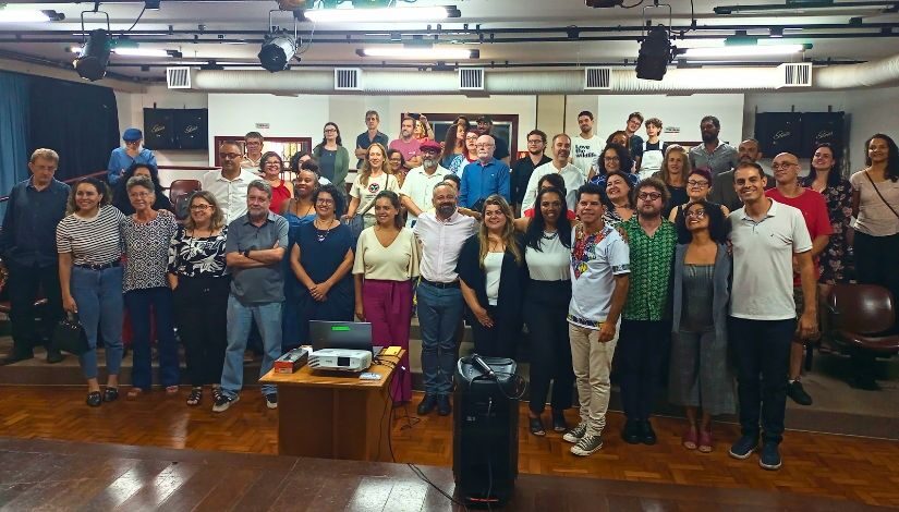 Fotografia mostra um grupo de pessoas posando para foto em auditório.