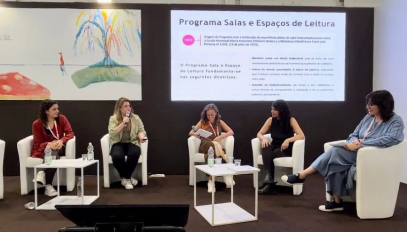 foto de mulheres sentadas, explicando o conteúdo projetado em duas telas ao fundo