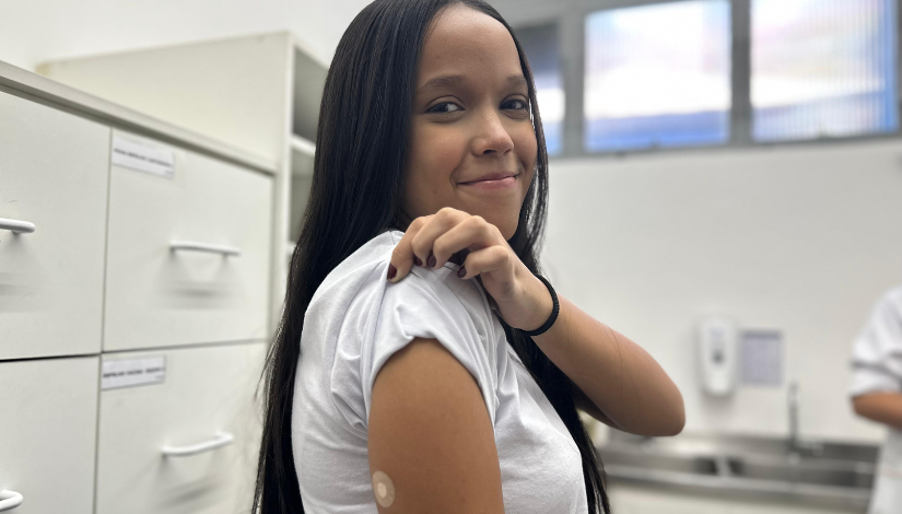 Uma adolescente sorri e mostra uma marca de vacina no braço