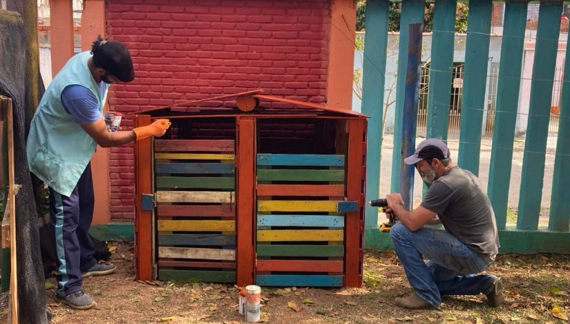 Fotografia mostra dois homens pintando uma estrutura de madeira.