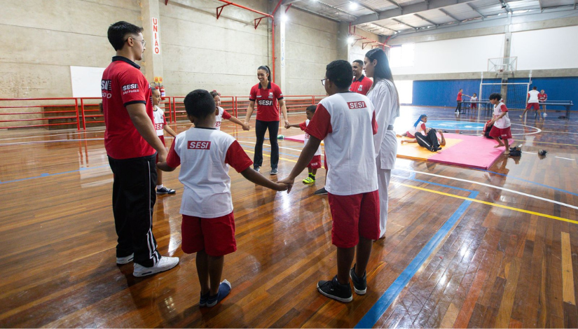 Uma quadra com cinco crianças e cinco adultos segurando as mãos em uma roda