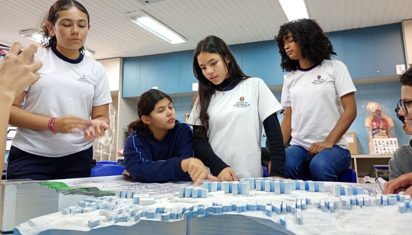 Fotografia de 5 estudantes em frente a uma maquete feita na impressora 3D do 