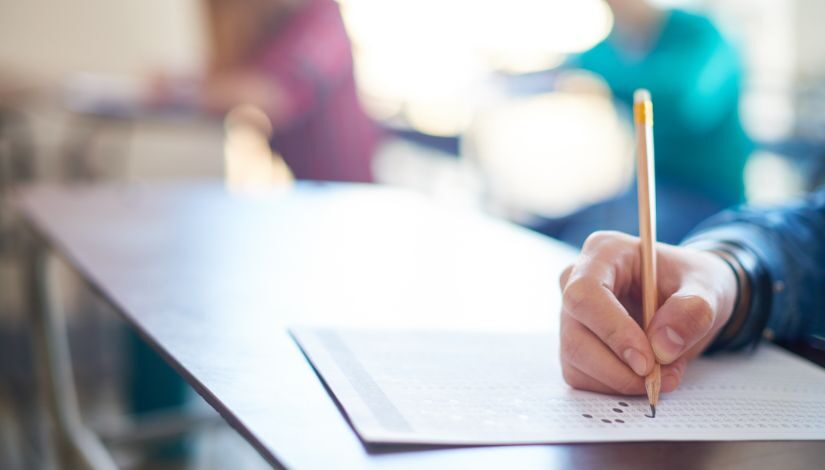 Fotografia de uma mão segurando um lápis sobre uma folha de respostas.
