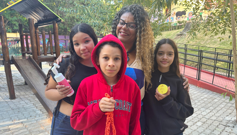 Um mulher posa para foto com três crianças, um menino com uma blusa vermelha e duas meninas com blusas pretas