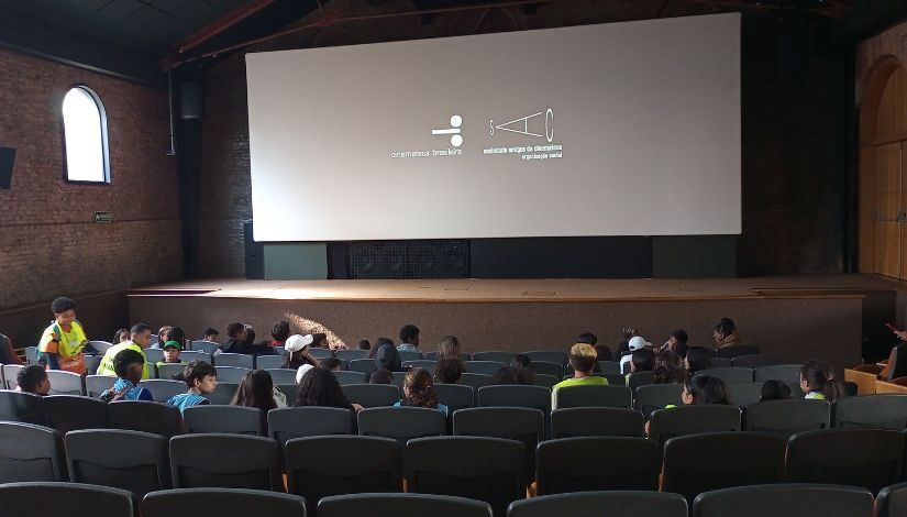 Fotografia tirada na Cinemateca Brasileira mostra crianças sentadas em sala de projeção.