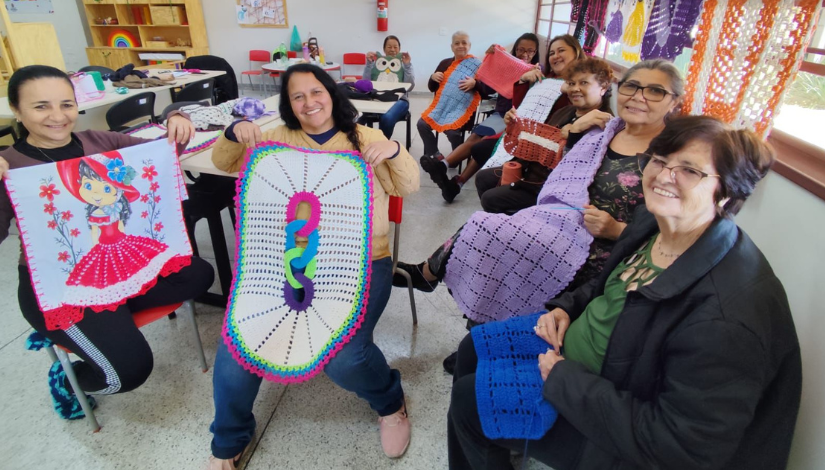 Fotografia mostra grupo de mulheres mostrando trabalhos feitos com crochê no projeto Crochetando Poesia