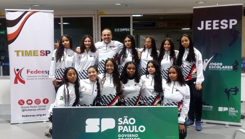 Fotografia mostra grupo de meninas e um professor posando para foto