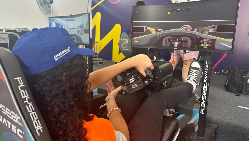 Uma estudante com colete laranja sentada em um simulador de corrida 