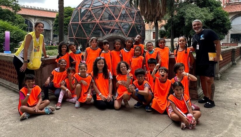 Grupo de jovens com coletes larnjas posando para a foto com um jardim de fundo