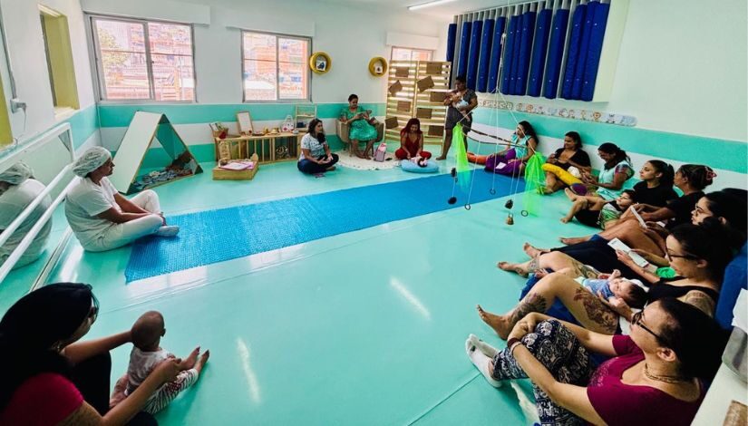 Fotografia mostra mulheres sentadas no chão encostadas nas paredes em uma sala.