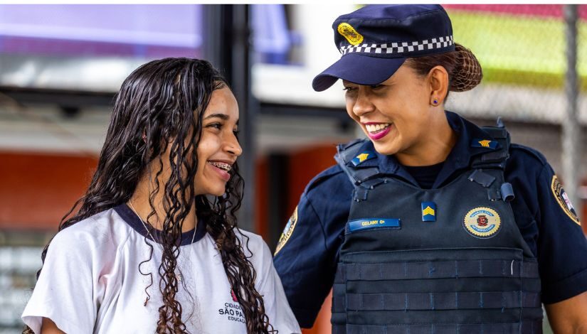 foto de uma estudante e uma guarda municipal, ambas se entreolham sorrindo